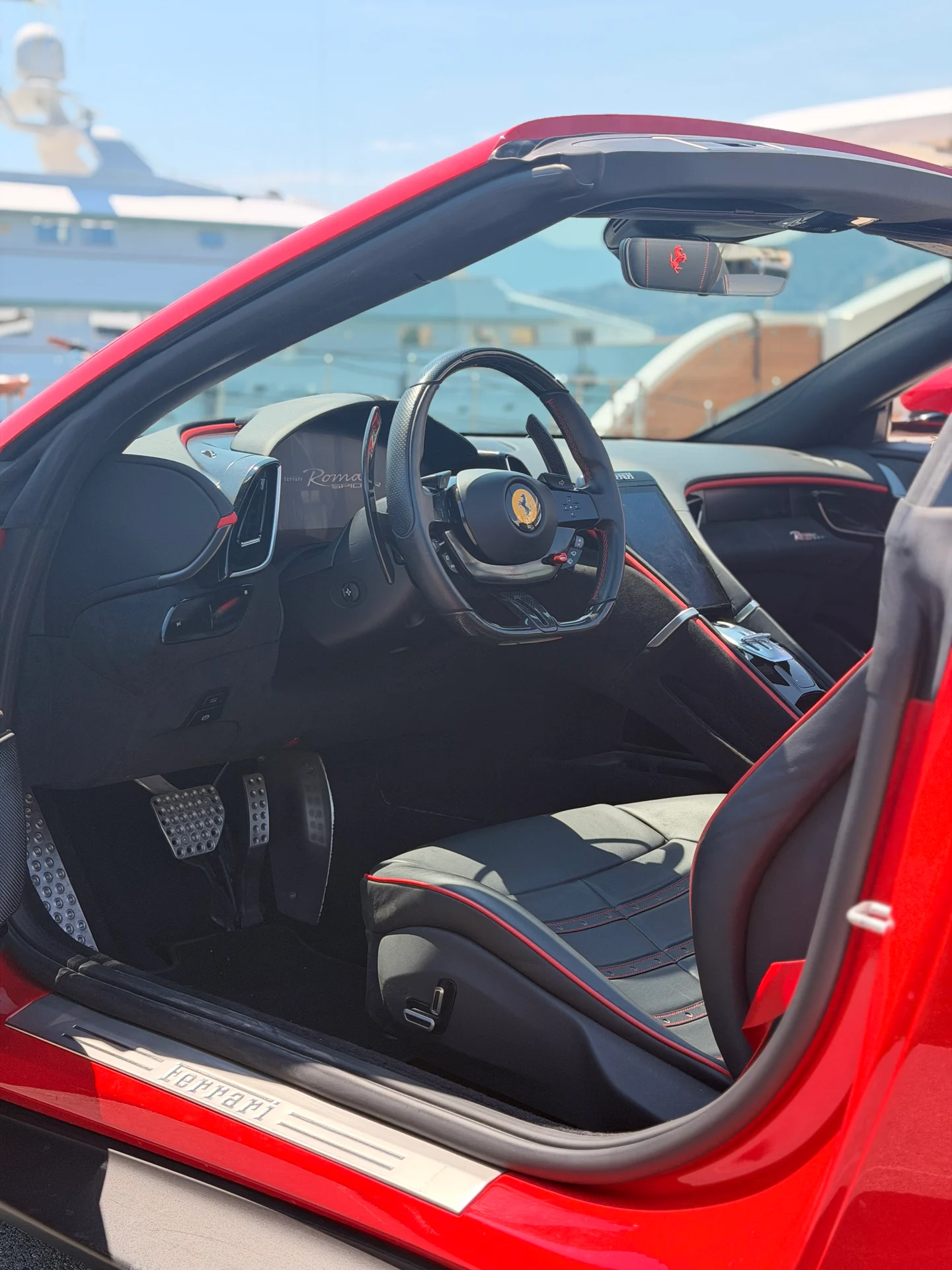 Dark Ferrari Roma Spider cabin with steering wheel, centre console and red seat accents.